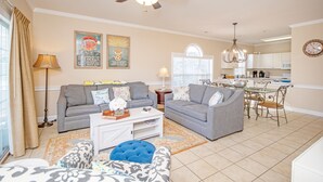 A living room with two grey sofas, a white coffee table, and a blue ottoman. There is a ceiling fan, a chandelier, and a dining area with a table and chairs. - A golf course view escape in the heart of Myrtle Beach! (Myrtle Beach)