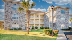 A multi-story building with a stone facade, balconies, and a well-maintained lawn. - A golf course view escape in the heart of Myrtle Beach! (Myrtle Beach)