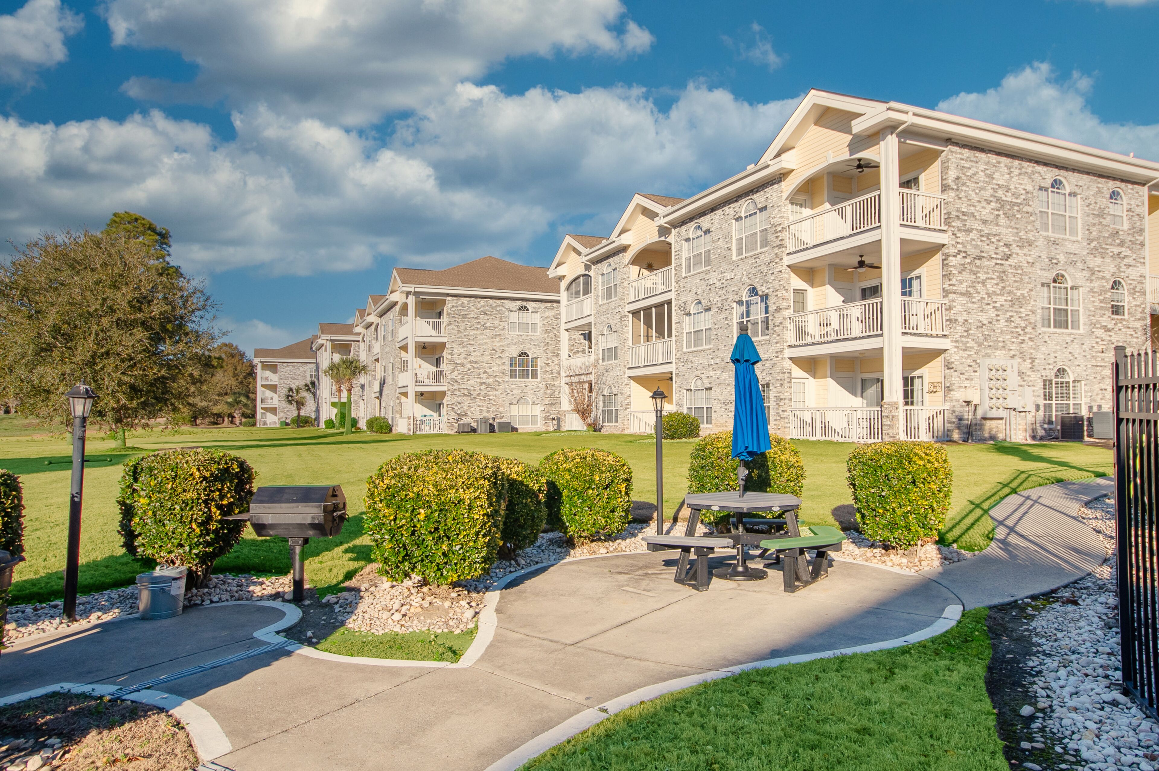 A multi-story building with stone facade, balconies, and a well-maintained lawn.