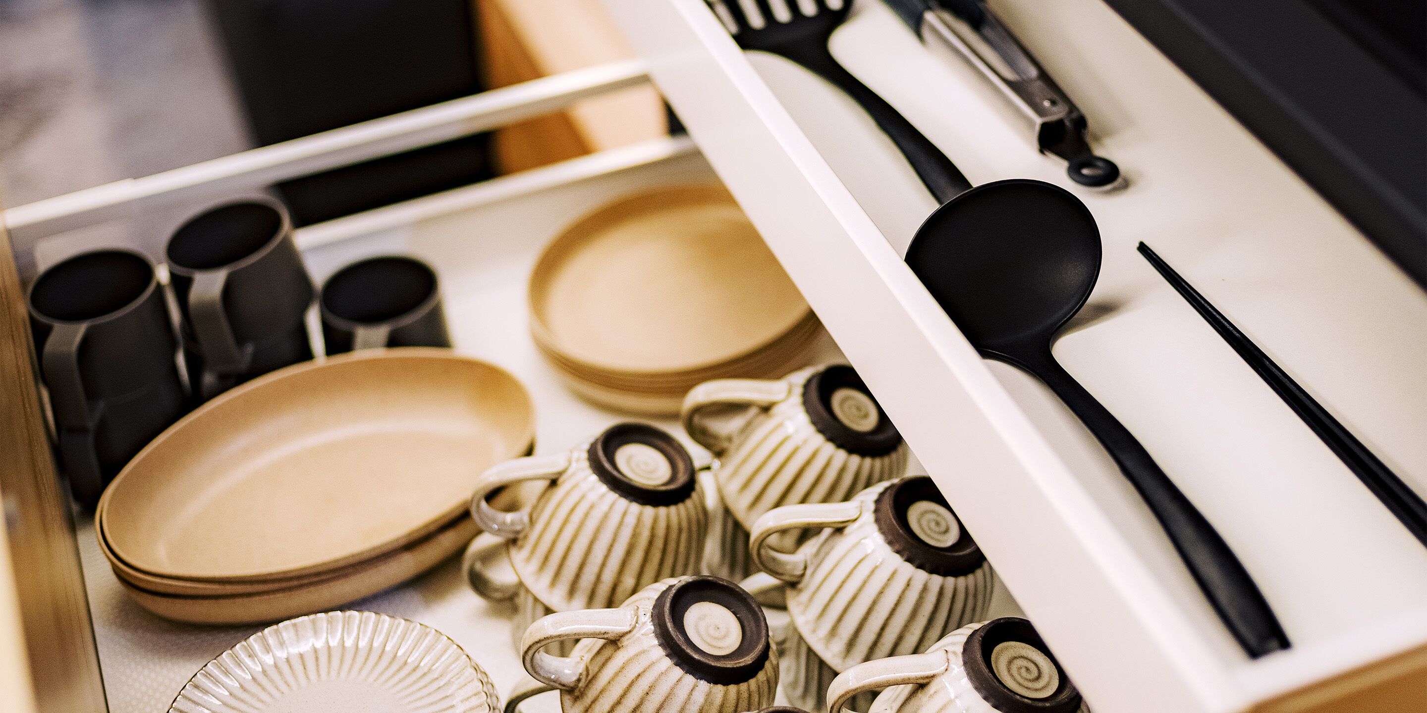 A drawer containing various kitchen utensils and dishes, including plates, cups, and a spatula.