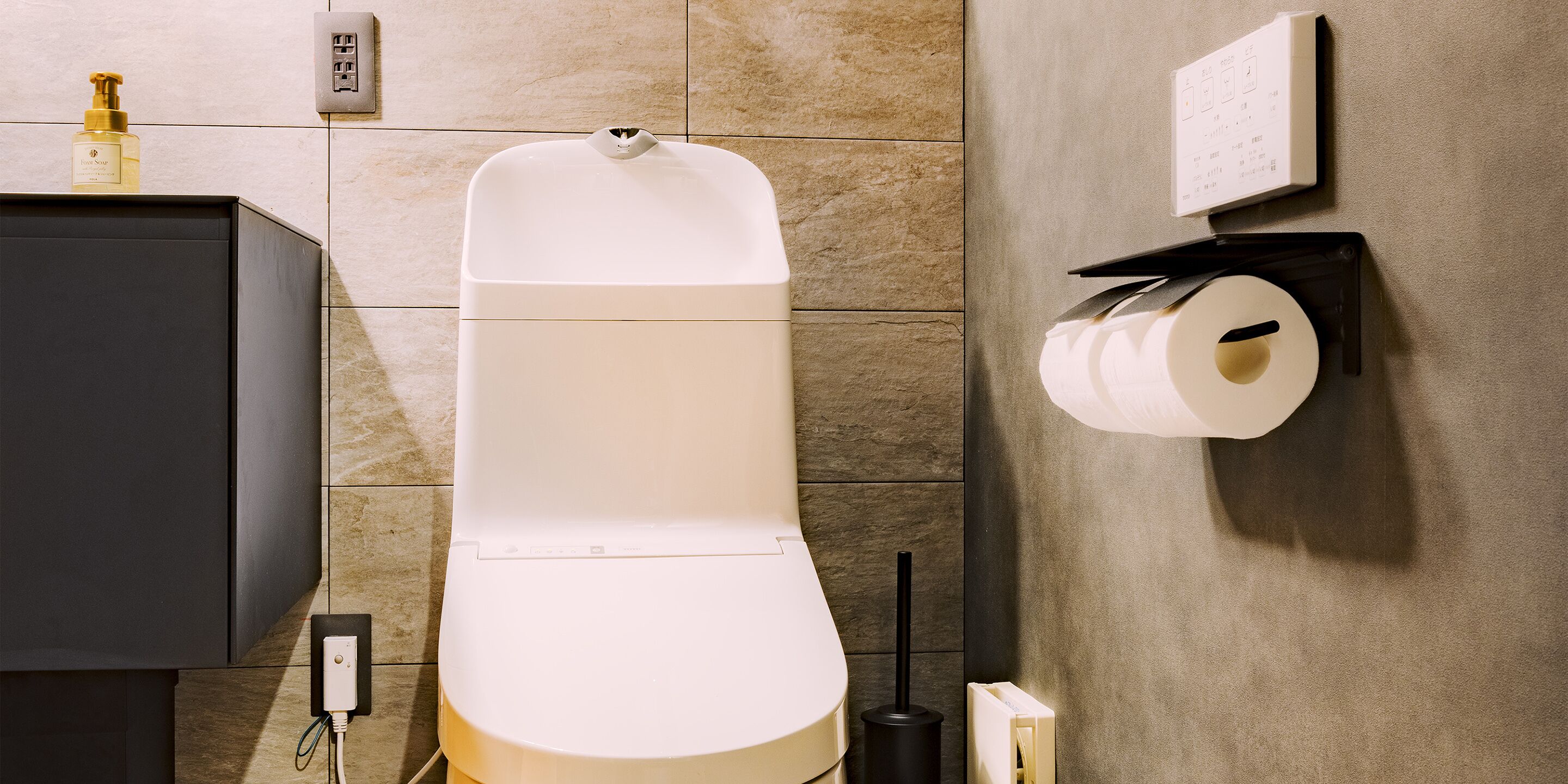 A modern bathroom with a toilet, a black cabinet, a wall-mounted toilet paper holder, and a soap dispenser.
