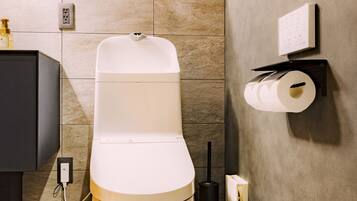 A modern bathroom with a toilet, a black cabinet, a wall-mounted toilet paper holder, and a soap dispenser.