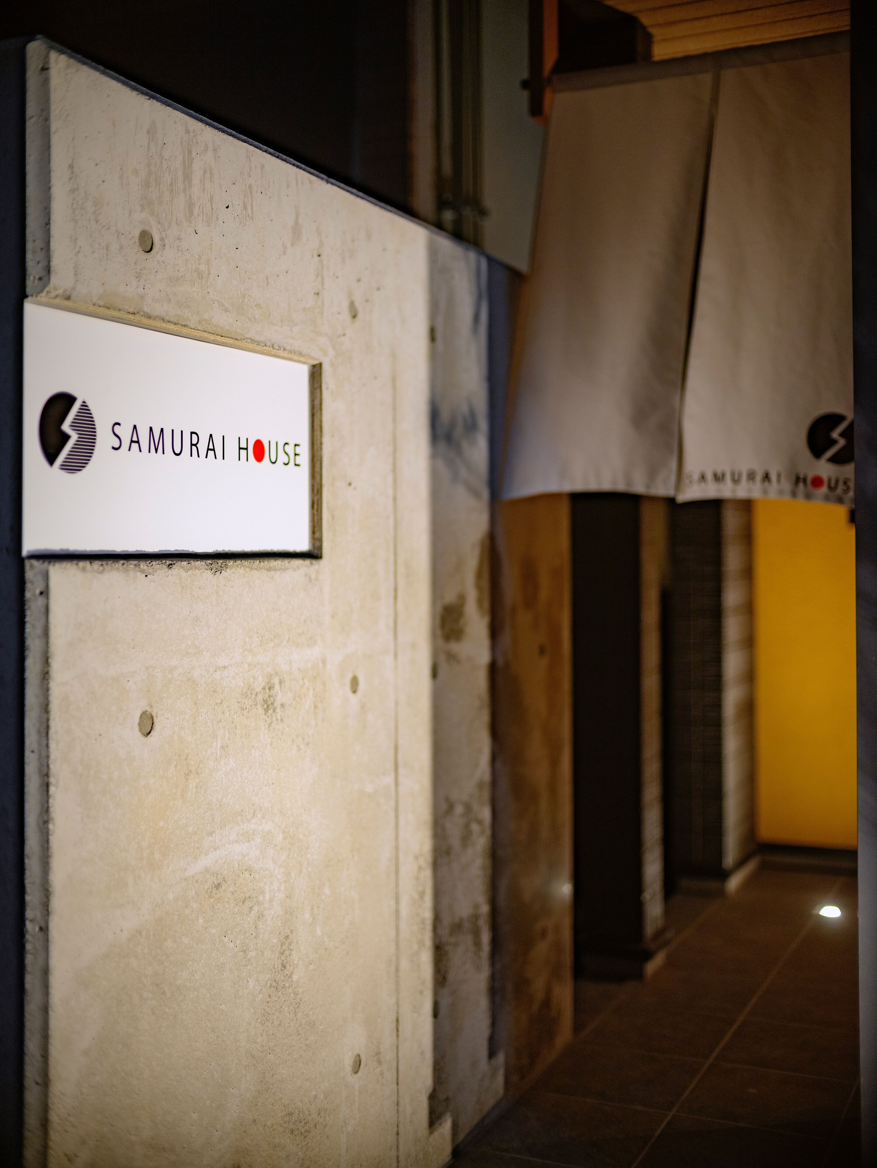 A sign for Samurai House, a building with a concrete exterior and a visible entrance.