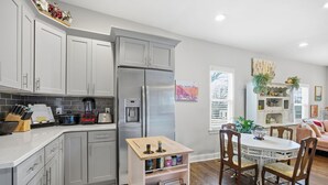 Une cuisine moderne avec des meubles gris, un réfrigérateur en acier inoxydable, une machine à café et une table en bois avec des chaises.