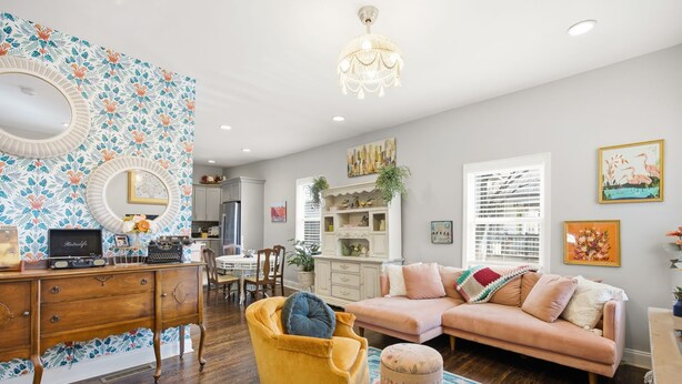 Un salon comprenant un canapé, un fauteuil et un pouf, une armoire en bois, un lustre et un mur orné d’un motif.