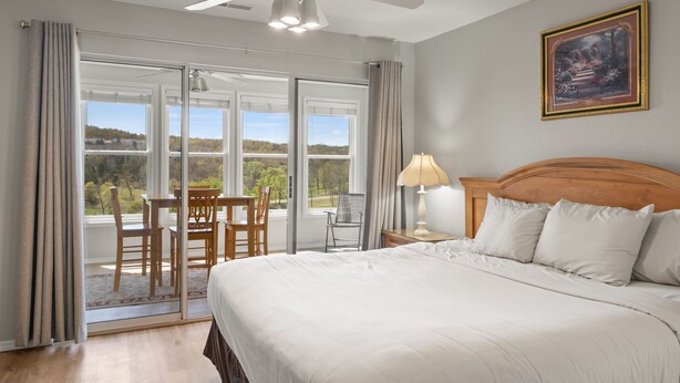 Een hotelkamer met een groot bed, een plafondventilator, een tafel met stoelen en uitzicht op het buitengebied door de glazen deuren.