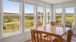Een eetkamer met een grote tafel en stoelen, grote ramen met uitzicht op een groen landschap.