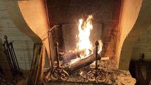 Une cheminée avec des bûches qui brûlent, un paravent en métal et un tisonnier en bois.