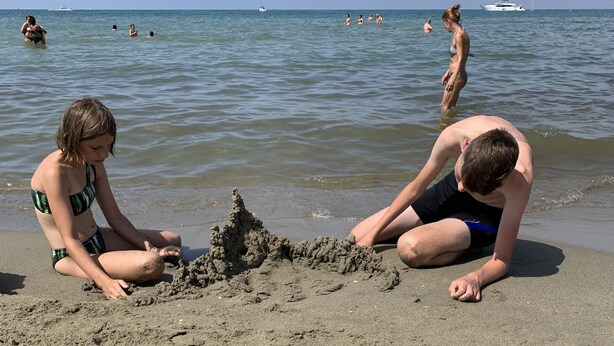 Een zandstrand met mensen die spelen en zandkastelen bouwen.