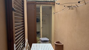 Een kleine buitenruimte met een witte tafel en twee witte stoelen, een bruine prullenbak en een plant in een pot.