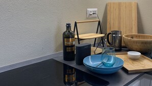 Een moderne keuken met een zwart aanrecht, een houten snijplank, een glazen kom, een metalen karaf en een fles wijn.
