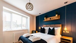 Une chambre moderne avec un grand lit, des tables de chevet, un luminaire suspendu et une fenêtre avec des stores.