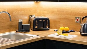 Une cuisine moderne avec un revêtement mural en bois, un évier en acier inoxydable, un grille-pain noir, une bouilloire et des citrons frais posés sur le plan de travail.