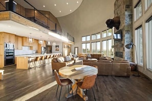 Een ruime woonkamer met een hoge plafond, een stenen openhaard en een groot raam dat natuurlijk licht binnenlaat.
