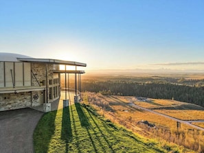 Ein modernes Gebäude mit gewölbter Dachform und Glasfassade, mit Blick auf eine hügelige Landschaft unter blauem Himmel.