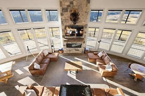 Amplia sala de estar con chimenea de piedra, sofás de cuero y ventanas grandes con vistas al exterior.