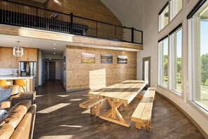 Ein geräumiger Raum mit einem großen Holztisch und Bänken, einer Küchenzeile und einem Balkon mit Geländer.