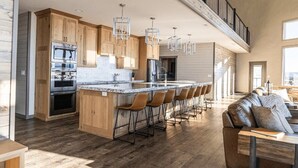 Une cuisine spacieuse avec des meubles en bois, un grand îlot central doté de tabourets et un éclairage moderne suspendu au plafond.