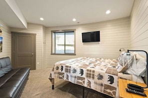 Un dormitorio con cama, televisor montado en la pared, ventana y puerta.