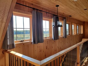 A wooden interior with multiple windows, a balcony railing, and a hanging light fixture.