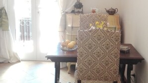 Un coin repas avec une chaise à motifs, une table sur laquelle se trouvent une théière et un pichet, et une vue à travers une porte vitrée.