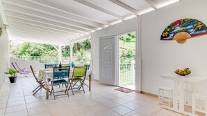 A covered patio with a table and chairs, a fan, and a door leading to a balcony.