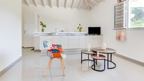 A modern kitchen with white cabinetry, a dining area with a round table and chairs, and a large window with a view of greenery.