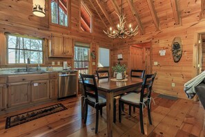 A wooden cabin interior with a dining table, chairs, a chandelier, and a kitchen area. - Misty Ridge by Mountain Oasis | True Log Cabin Rental Near Blue Ridge & Ellijay (Blue Ridge)