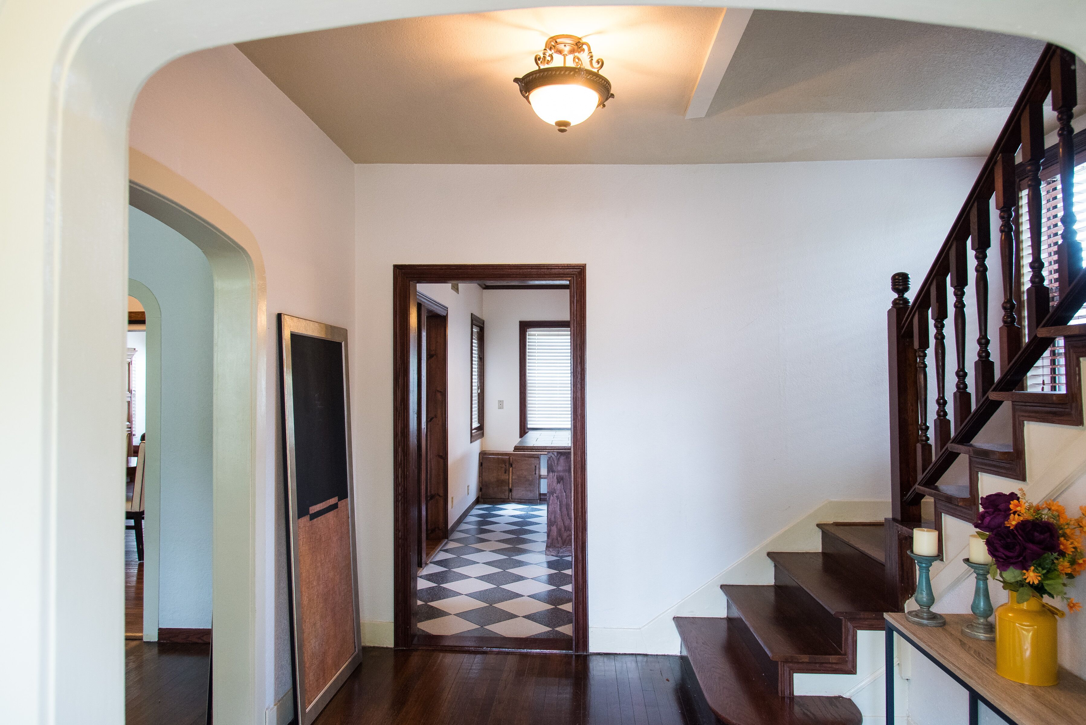 A hallway with a checkered floor leading to a staircase with wooden steps and a railing.