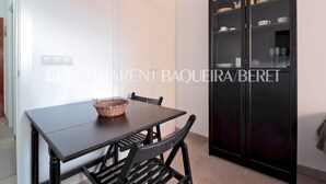 A dining area with a dark wooden table and chairs, a wicker basket, and a black cabinet with glass doors containing dishes and cups. - Saburedo - Edificio Saumet (Baqueira)