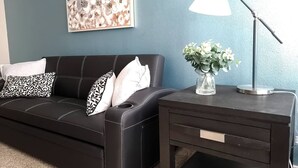 Un canapé en cuir foncé agrémenté de coussins à motifs, un vase rempli de fleurs et une lampe de bureau, le tout placé devant un mur bleu.