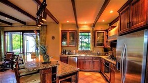 A spacious kitchen with wooden cabinets, a large island, and a stainless steel refrigerator. - Casa Orchidea (Tamarindo)