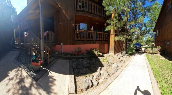 A wooden cabin with a balcony, a stone pathway, and a car parked in front.