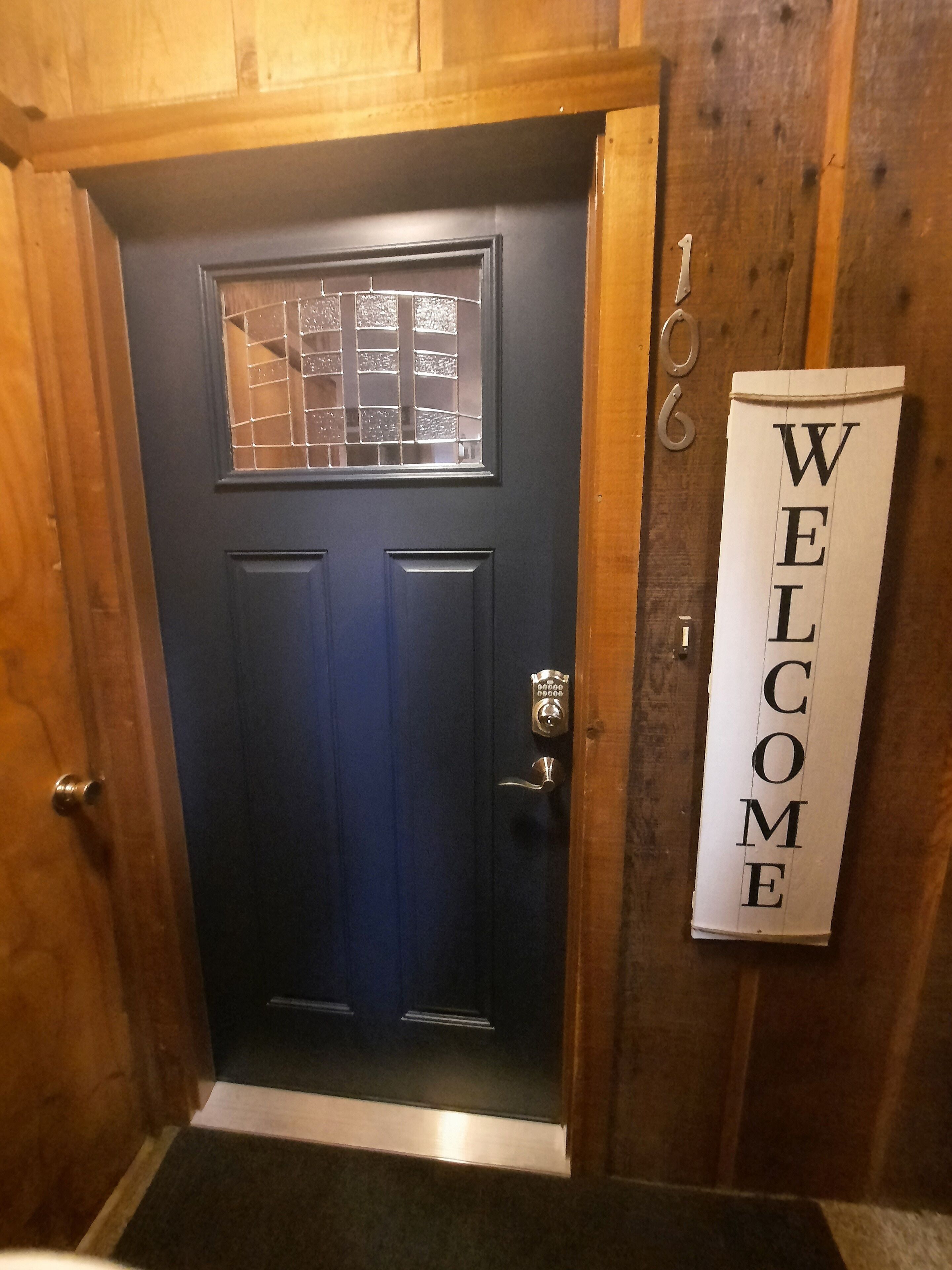 Una puerta azul oscuro con una ventana, un timbre y un letrero que dice 'WELCOME'.