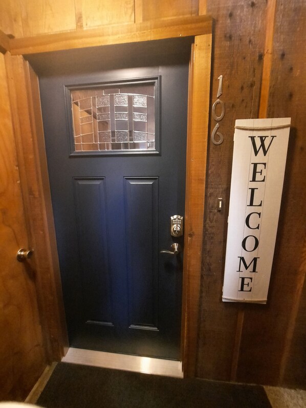 Una puerta azul oscuro con una ventana, un timbre y un letrero que dice 'WELCOME'.