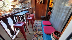 Un pequeño espacio al aire libre con mesas de madera, taburetes rojos, una alfombra con estampado colorido y una planta en maceta.