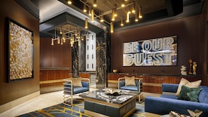 Un vestíbulo moderno con una mesa de centro de mármol, sofás azules y un letrero que dice 'Be Our Guest'.