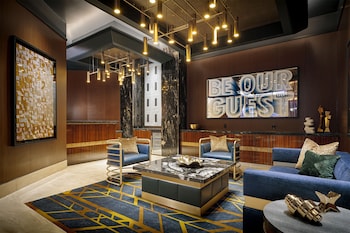 A hotel room with a large bed, a blue sofa, a small table, and a view of the city at night. at Circa Resort & Casino – Adults Only