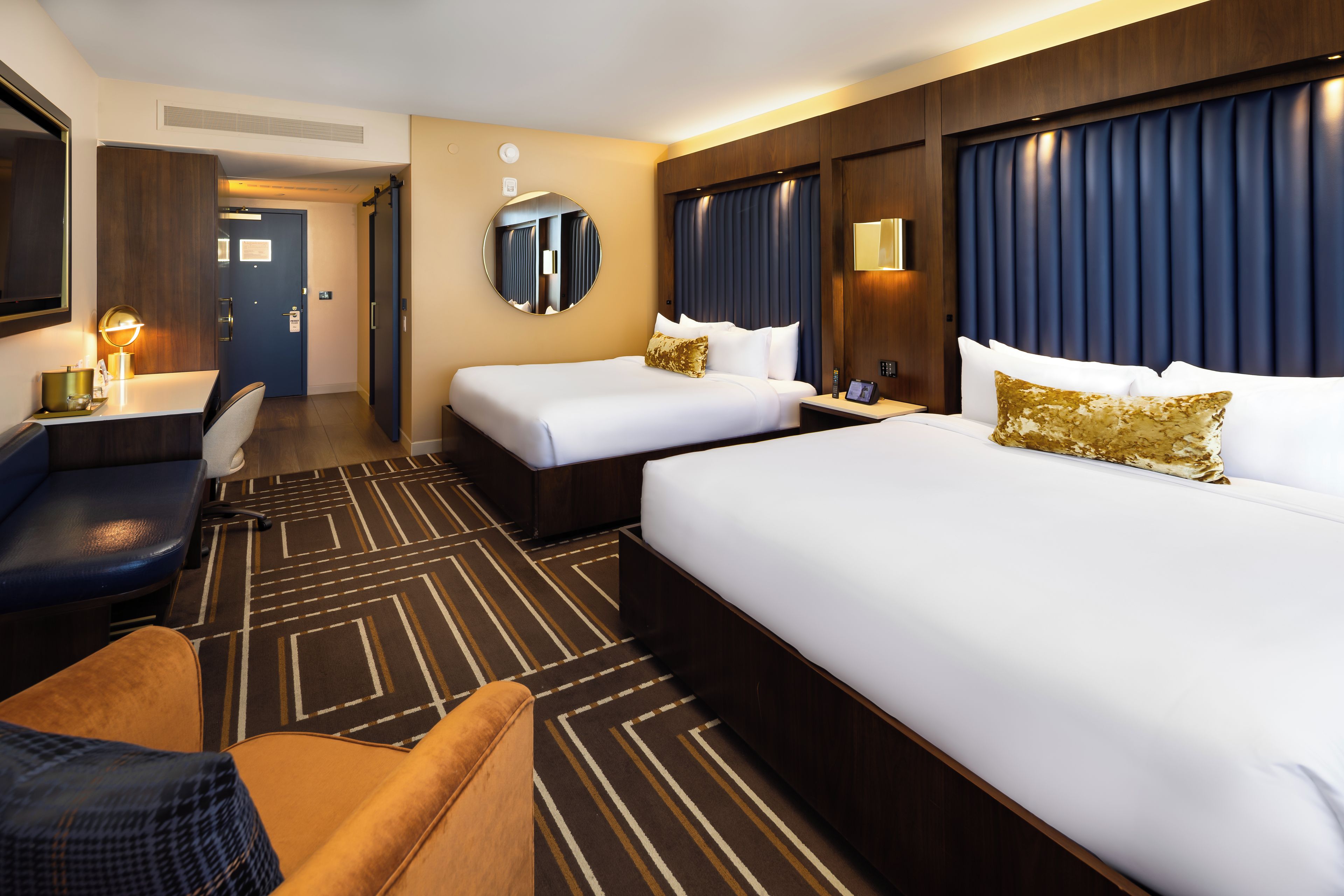 Ein Hotelzimmer mit zwei Betten, einem Schreibtisch, einem Stuhl und einem großen Spiegel.