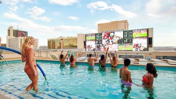A swimming pool with a cityscape in the background, including a large screen displaying sports events.