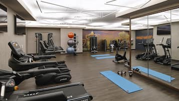 A modern gym with exercise equipment, blue mats, and a large mirror.
