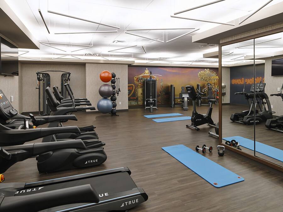 A modern gym with exercise equipment, blue mats, and a large mirror.
