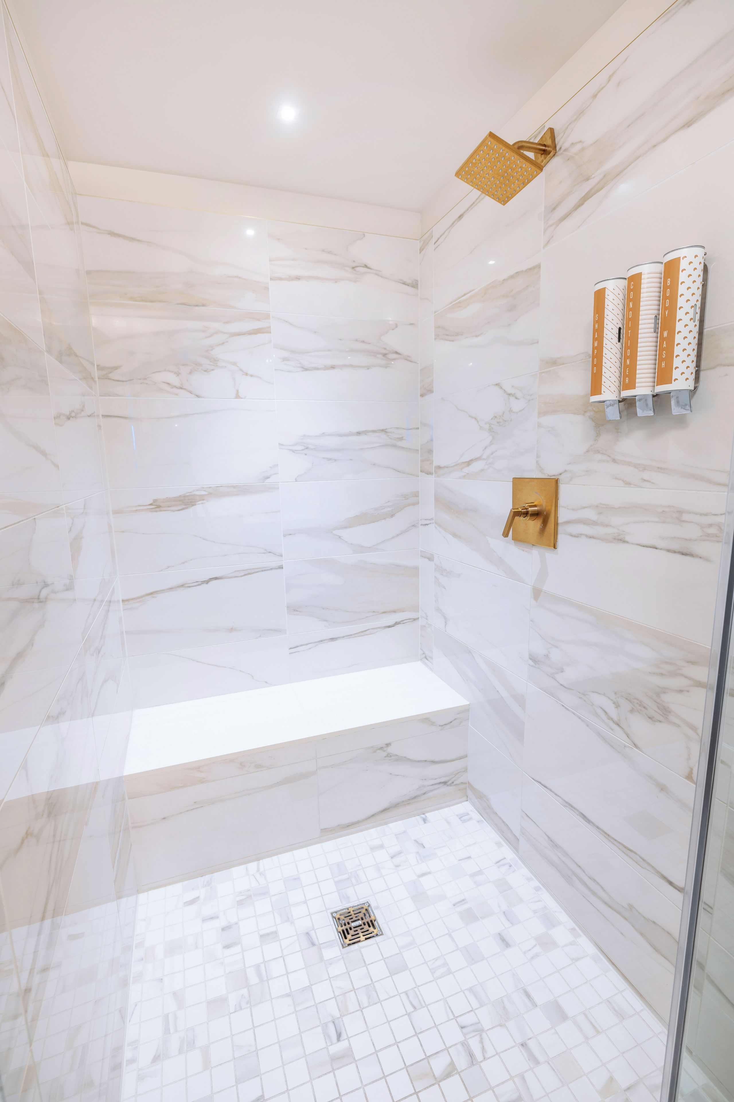 A modern bathroom with marble walls, a glass shower enclosure, and a built-in bench.