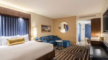 Une chambre d’hôtel avec un grand lit, un canapé bleu, une petite table ronde et un miroir.