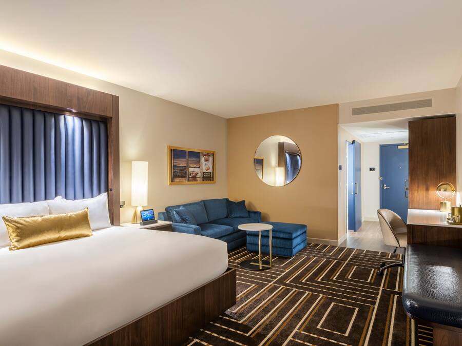 Une chambre d’hôtel avec un grand lit, un canapé bleu, une petite table ronde et un miroir.