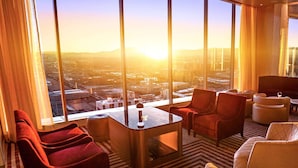 A modern hotel room with a large window offering a city view, a comfortable seating area with red and white chairs, and a small table. - Circa Resort & Casino – Adults Only (Las Vegas)