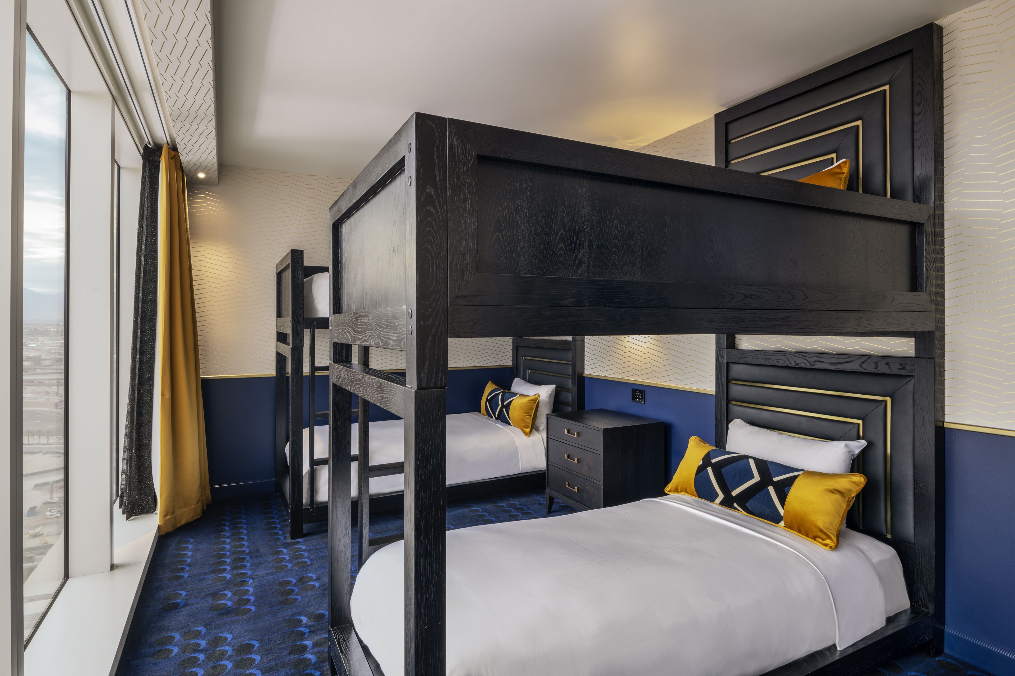 A room with bunk beds, a desk, and a view through large windows.