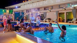Zona de piscina con vistas al letrero 'STADIUM SWIM', sillones de descanso y un área de estar con un muro estampado.