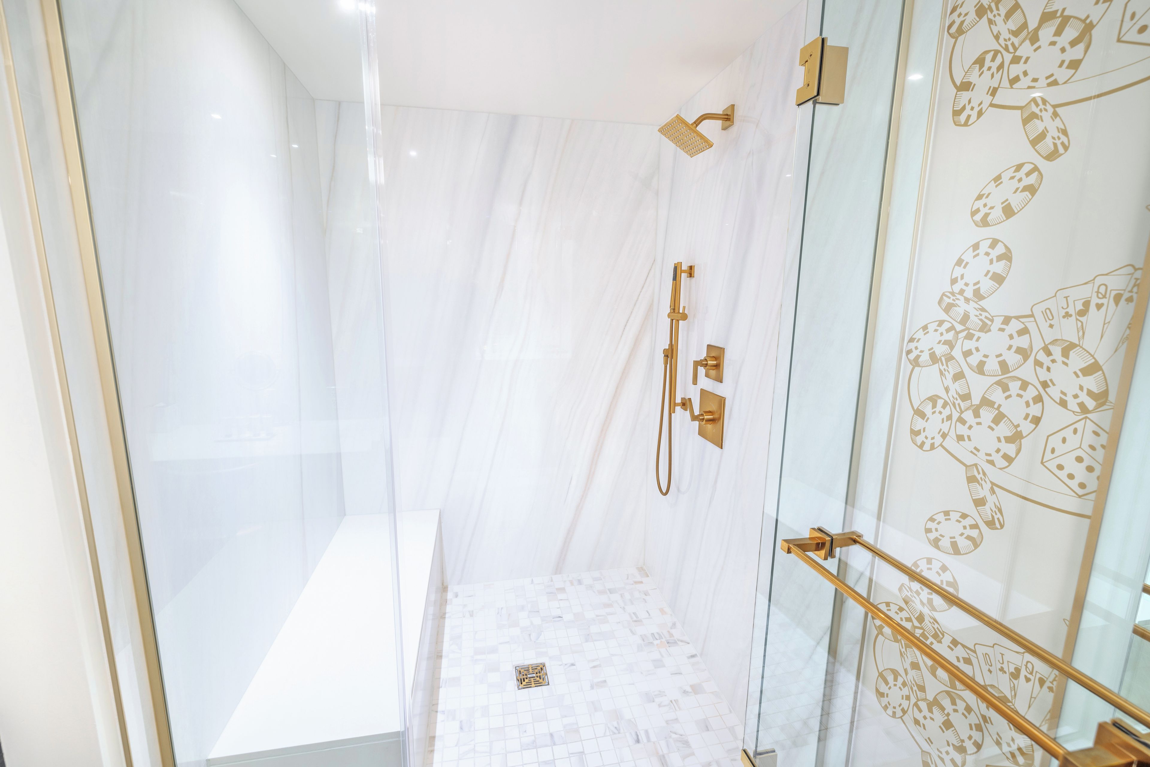 Een moderne douche met een glazen douchecabine, gouden details en een marmeren wand.