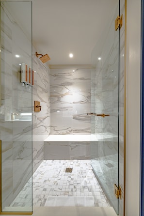 A modern bathroom with a glass shower enclosure, marble walls, and a tiled floor.